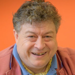 Rory Sutherland speaker agent photo as Rory in pink jacket smiles to camera in headshot crop.
